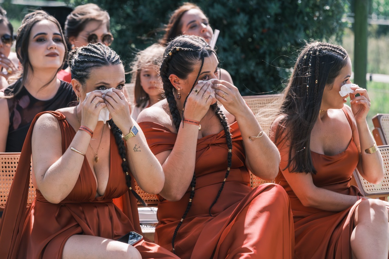Convidadas sentadas ao ar livre a limpar as lágrimas durante a cerimónia de casamento. Foto documental por Filipe Santos, 2025.